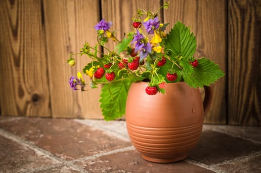 Ripe strawberries and a bouquet of forest flowers in a clay mug