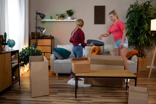 Two friends unpack boxes in a stylish living room filled with plants and furniture, creating a vibrant vibe