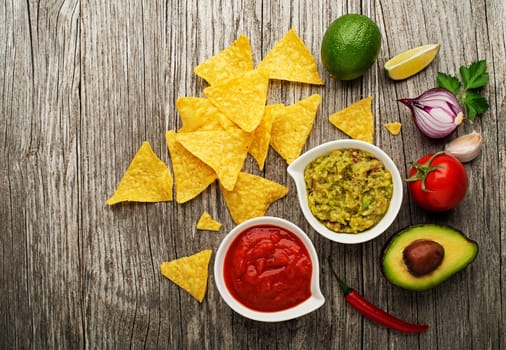 Avocado guacamole and tomato salsa with fresh ingredients on table
