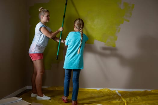 A mother and daughter joyfully paint a wall together in their cozy home, demonstrating teamwork and collaboration