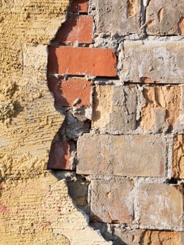 Format-filling view of old masonry with partially detached rough plaster and clinker bricks.