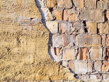 Format-filling view of old masonry with partially detached rough plaster and clinker bricks.