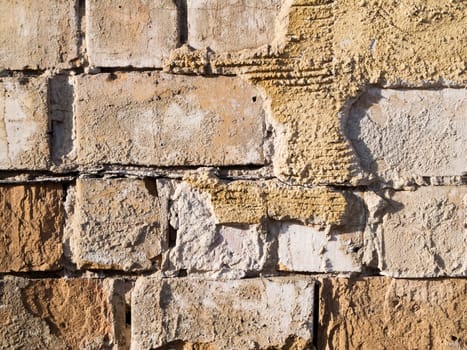 Format-filling view of old masonry with partially detached rough plaster and clinker bricks.