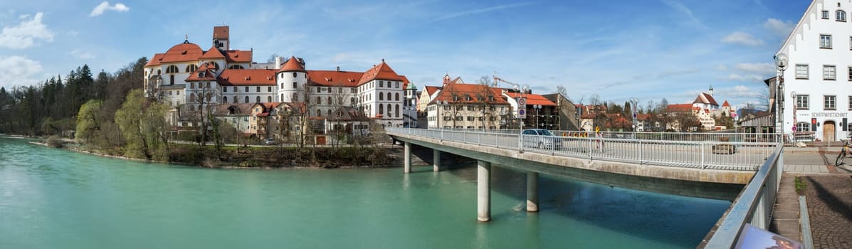 Füssen,Germany - April 10,2016: Panoramic view of the parish church of St. Mang,city museum,town hall and Benedictine monastery of St. Mangder of the city of Füssen. Panoramic view over the river Lech to the city of Füssen with the architectural complex Stadtpfarrkirche St. Mang,Stadt-Museum,Rathaus and Benediktinerkloster St. Mangder Stadt Füssen as well as the Lechhalde Bridge leading to the old town in summer 2016.