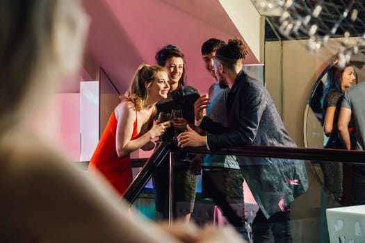 Friends are standing in a nightclub together drinkiong cocktails while they chat.