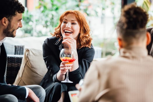Business people are enjoying drinks together in a bar couryard after work. They are laughing and talking while drinking cocktails.