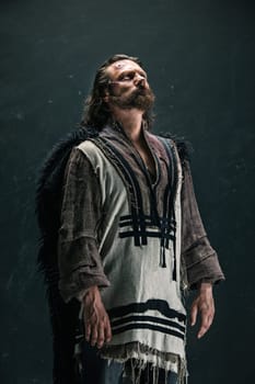 Actor in makeup, a poor man on black studio background. The bum in canvas rags. concept of vagrancy and survival