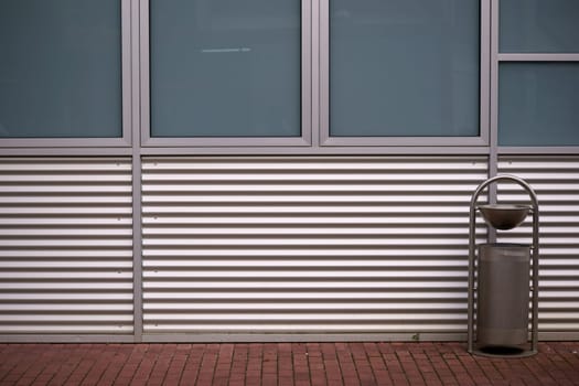The sheet metal cladding of a modern building in front of which stands a trash can.