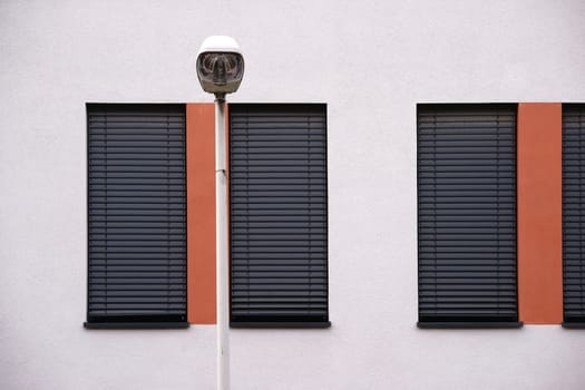 The modern façade of a modern residential building with windows with metal blinds and street lighting.