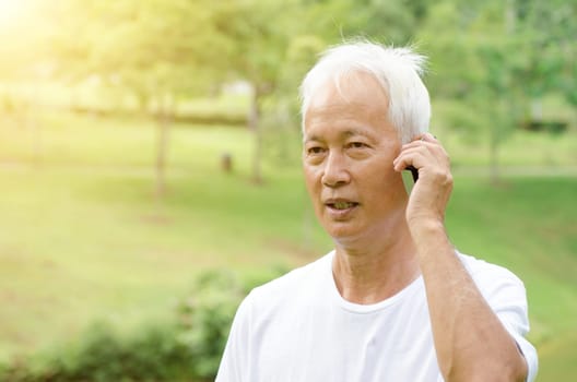 Portrait of gray hair Asian old man calling on smart phone, standing at outdoor park in morning.