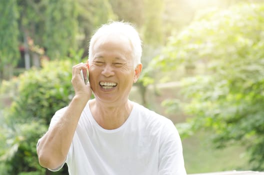 Portrait of happy gray hair Asian old man talking on smart phone, at outdoor park in morning.