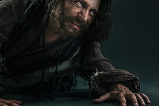 Actor in makeup, a poor man on black studio background. The bum in canvas rags. Concept of vagrancy and survival. Concept of pain and suffering. The wounded man crawling to salvation
