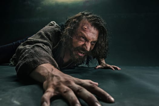 Actor in makeup, a poor man on black studio background. The bum in canvas rags. Concept of vagrancy and survival. Concept of pain and suffering. The wounded man crawling to salvation