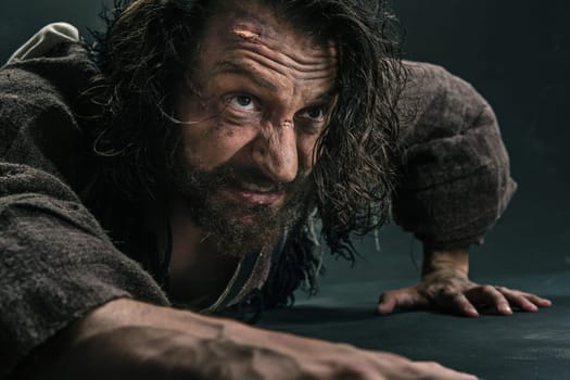 Actor in makeup, a poor man on black studio background. The bum in canvas rags. Concept of vagrancy and survival. Concept of pain and suffering. The wounded man crawling to salvation