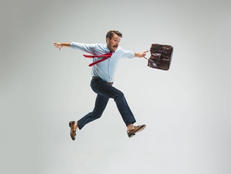 Businessman running with a briefcase, isolated on gray studio background