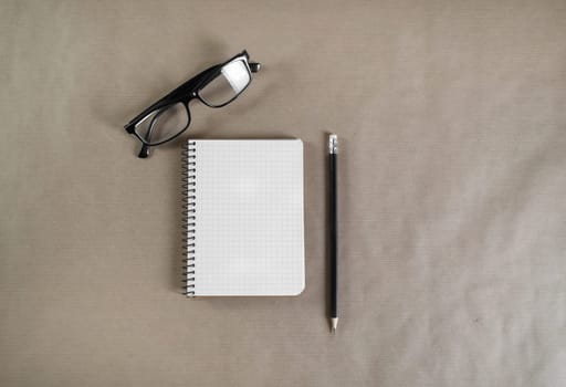 Photo of blank notebook, glasses and pencil on craft paper background. Top view.