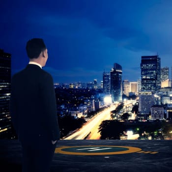 Business man standing on rooftop helipad. Looking at the city. Business success concept