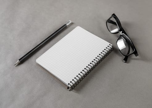 Blank notepad, glasses and pencil on craft paper background. Stationery elements. Responsive design mockup.
