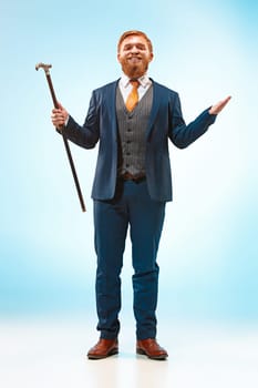 The bearded man in a suit holding cane. Isolated on a blue background.