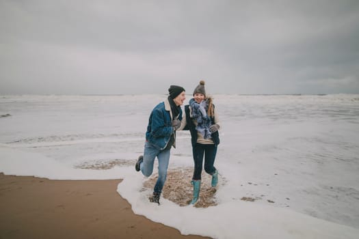 A young couple laugh and paddle in the sea on a winter beach.