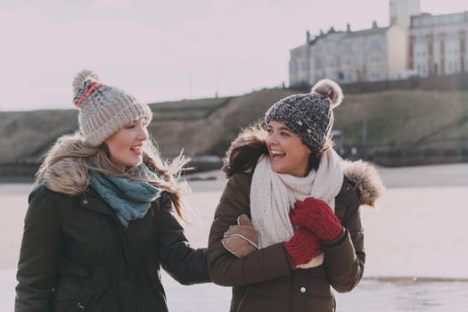 Two women laughing on a winter beach.