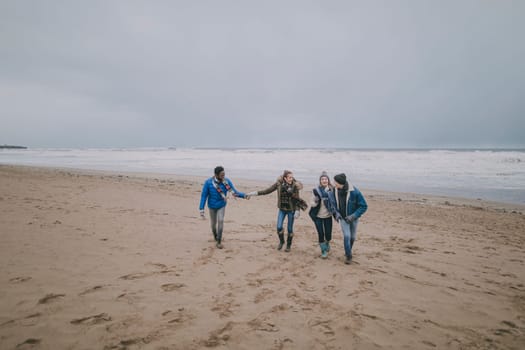 Two couples talk and laugh together whilst walking along a beach in winter.