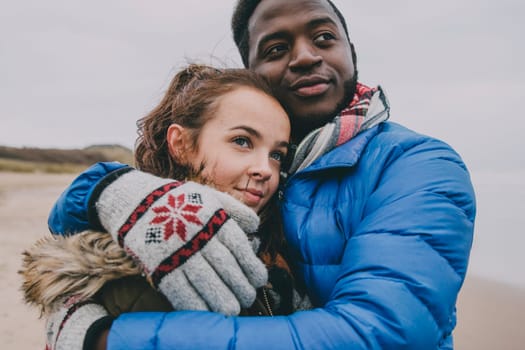 A young couple hug and look into the distance on a winter beach.