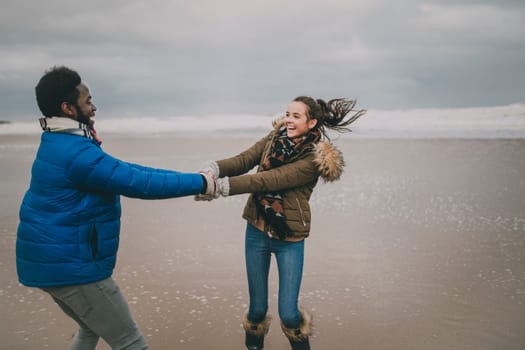 A young couple laugh and dance on Tynemouth beach in winter.