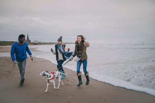 Three friends walk a dog along Tynemouth beach in winter.