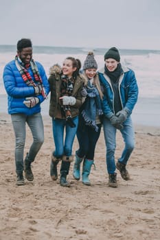A group of friends talking and laughing whilst walking along a winter beach.