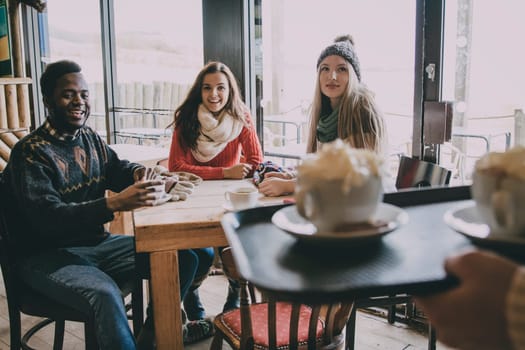 A group of teenagers happy to see their coffee being served in a cafe in winter.