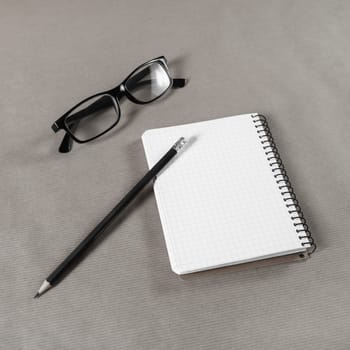 Blank notebook, glasses and pencil on craft paper background.
