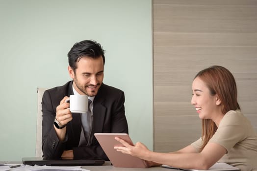 beautiful young asian business woman and caucasian man look at tablet for business project