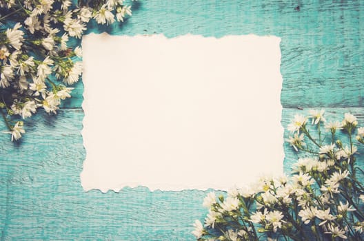 White flowers and paper card on blue wooden background. Festive greeting card top with copy space, flat lay. Vintage tone filter.