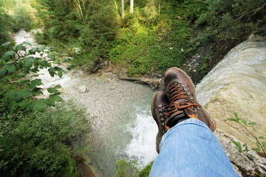 Young man at a waterfall,you can see the mountain boots