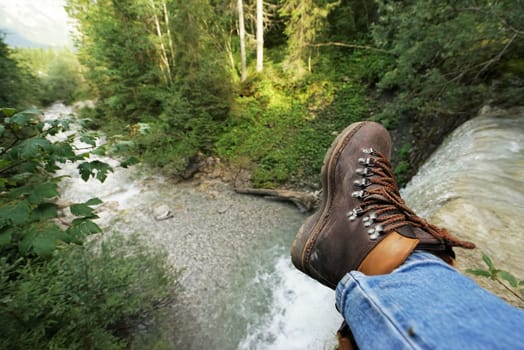 Young man at a waterfall,you can see the mountain boots