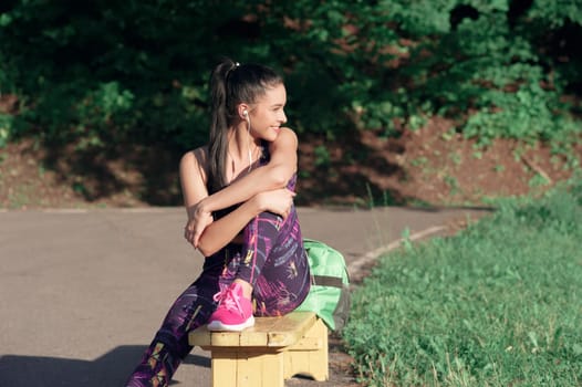 Sports and lifestyle concept - young brunette woman resting after sports smiling sitting on a bench, outdoors