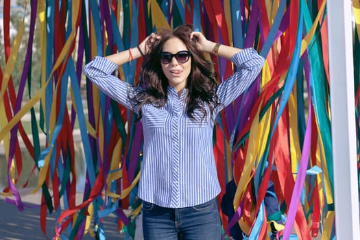 portrait of a young beautiful woman in dark glasses on a summer sunny day against the background of colorful ribbons in the park on vacation.