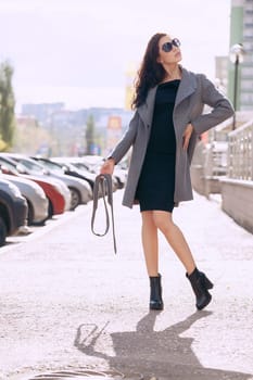 Outdoor portrait of a young beautiful fashionable woman, outdoors. A model dressed in a stylish gray coat, sunglasses. The concept of women's fashion, urban lifestyle.