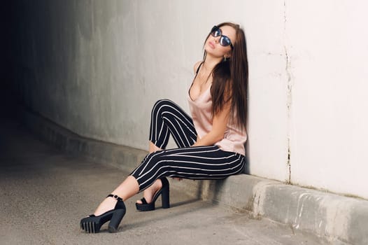 Outdoor portrait of a young beautiful fashionable happy lady, wearing sunglasses, in a wooden frame, creating a city on the street. The model wears stylish clothes. The girl is looking up, the hair is developing in the wind. Women's fashion. Urban way of life.