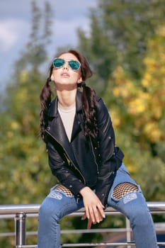 fashionable young woman in rock style clothes, black leather jacket, blue jeans, tights in a grid under battered jeans.