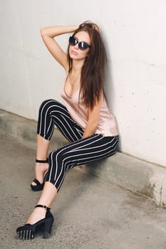 Outdoor portrait of a young beautiful fashionable happy lady, wearing sunglasses, in a wooden frame, creating a city on the street. The model wears stylish clothes. The girl is looking up, the hair is developing in the wind. Women's fashion. Urban way of life.