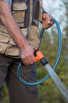 Senior man watering plants in his garden. Retired gardener watering the garden with hose. Happy older man gardening.