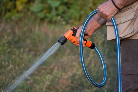 Senior man watering plants in his garden. Retired gardener watering the garden with hose. Happy older man gardening.