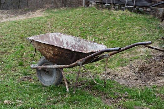 Old and well used rusty wheelbarrow in a village garden.