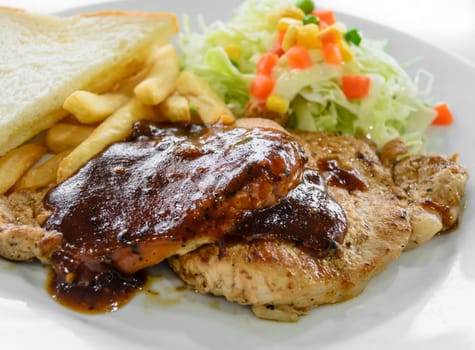 Grilled pork steak fillet with black pepper sauce, vegetable salad, bread and french fries on white plate