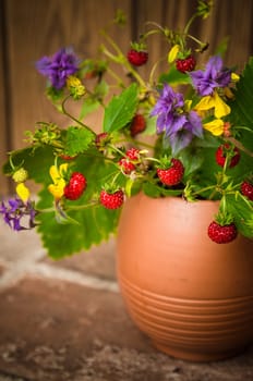 Ripe strawberries and a bouquet of forest flowers in a clay mug