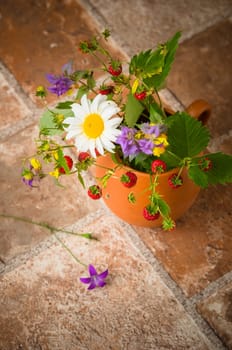 Ripe strawberries and a bouquet of forest flowers in a clay mug