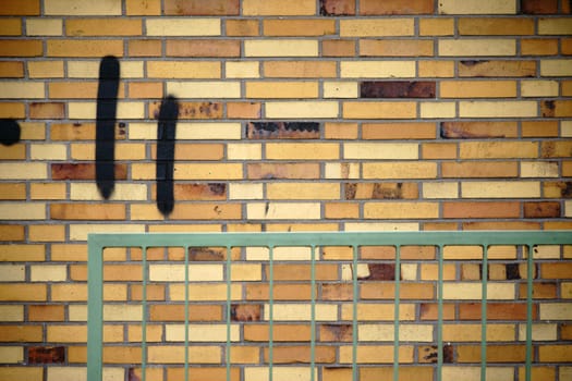 A wall of old clinker bricks with an angular railing in front of it.
