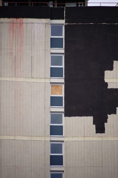 The side view of a high-rise building with a tiled façade and color repairs of damaged areas.
